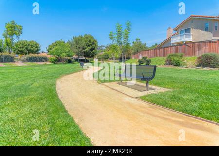 Parken Sie in einer Wohnanlage in San Diego, Kalifornien. Es gibt einen gebogenen Feldweg mitten im grünen Rasen und ein eingezäuntes Haus auf der rechten Seite. Stockfoto