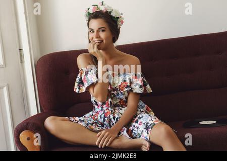 Glückliche Frau in schönem Kleid sitzt auf dem Vintage-Sofa Stockfoto