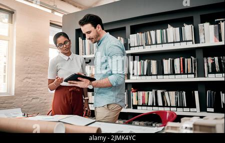 Es gibt sogar Apps für das Design. Zwei aufstrebende junge Architekten, die ein digitales Tablet nutzen, während sie in einem modernen Büro zusammenarbeiten. Stockfoto