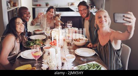 Es wäre nicht die festliche Jahreszeit ohne gute Freunde. Eine Gruppe junger Freunde, die während einer Dinner-Party zu Hause Selfies machen. Stockfoto