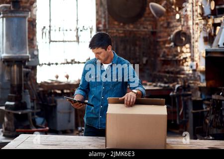 Ich erwarte heute mehr Lieferungen. Ein junger Geschäftsmann, der mit einem digitalen Tablet Bestellungen und Lieferungen in seiner Werkstatt sortiert. Stockfoto
