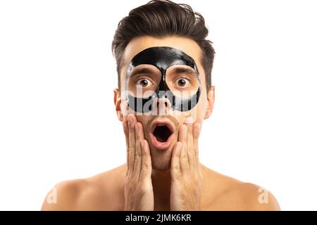 Junger Mann mit einer schwarzen Holzkohlemaske auf seinem Gesicht auf weißem Hintergrund. Stockfoto
