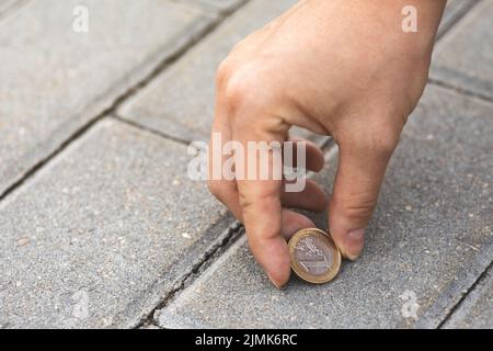 Weibliche Hand, die eine Euro-Münze vom Boden pflückt Stockfoto