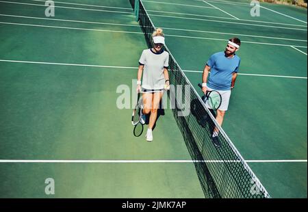 Auf welcher Seite sind Sie? In voller Länge ein Bild von zwei jungen Tennisspielern, die sich unterhalten, während sie gemeinsam auf einem Tennisplatz im Freien spazieren gehen. Stockfoto