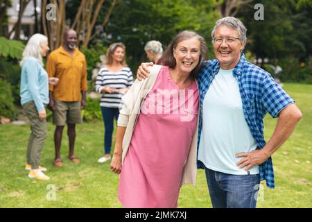 Porträt eines glücklichen kaukasischen älteren Paares mit multirassischen Freunden im Hintergrund Stockfoto