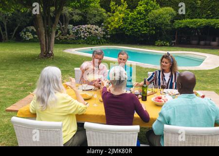 Mehrrassische ältere Männer und Frauen, die während der Hinterhofparty Essen am Tisch essen Stockfoto