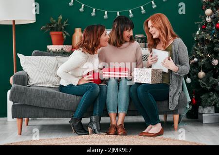 Meine Freunde, meine Schwestern. Drei attraktive Frauen tauschen Weihnachtsgeschenke auf dem Sofa zu Hause aus. Stockfoto