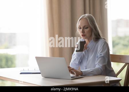 Seriöse, konzentrierte ältere Geschäftsfrau, die eine Sprachnachricht aufzeichnet Stockfoto