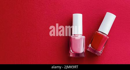 Rote und rosa Nagellackflaschen auf rotem Hintergrund, Maniküre und Kosmetik Stockfoto