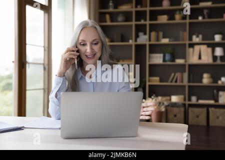 Ältere Geschäftsfrau, die vom Heimbüro aus arbeitet und mit dem Mobiltelefon spricht Stockfoto