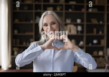 Glücklich attraktive ältere ältere Dame macht Finger Herz geformte Hände Stockfoto