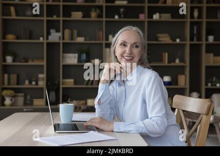 Fröhlich glücklich ziemlich ältere freiberufliche Geschäftsfrau, die vom Tisch wegschaut Stockfoto