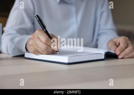 Geschäftsfrau mittleren Alters trägt blassblaues Hemd und schreibt Notizen Stockfoto