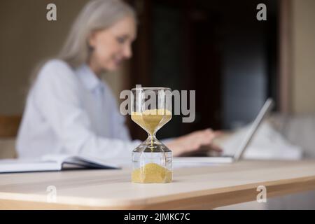 Sanduhr mit fließendem Sand auf dem Schreibtisch einer älteren Geschäftsfrau Stockfoto