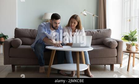 Seriöse Millennials-Paare sitzen auf dem Sofa und sortieren Papiere aus Stockfoto