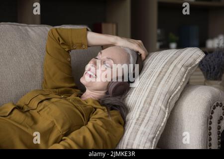 Fröhliche, friedliche, ältere Frau, die Kopfhörer trägt und Musik hört Stockfoto