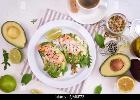 Frisch zubereitete Avocado-, Lachs- und Frischkäse-Toasts auf einer weißen Keramikplatte Stockfoto