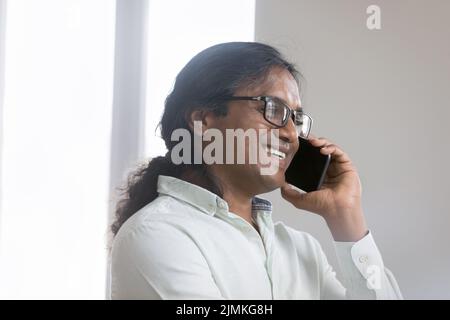 Lächelnder indischer Geschäftsmann spricht auf dem Smartphone Lösen Sie Geschäfte aus der Ferne Stockfoto