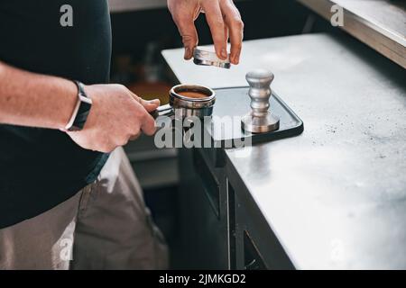 Barista hält den Sabotagekontakt und drückt gemahlenen Kaffee in den Halter, um Espresso für den Kunden zuzubereiten Stockfoto