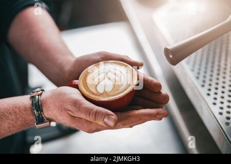 Nahaufnahme von Barista-Händen, die im Café frisch zubereiteten Cappuccino oder Latte-Becher halten Stockfoto