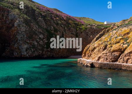 Idyllische Bucht mit kleinem Strand auf einer kleinen atlantischen Insel wirth Klippen und vielen bunten Blumen unter einem blauen Himmel Stockfoto