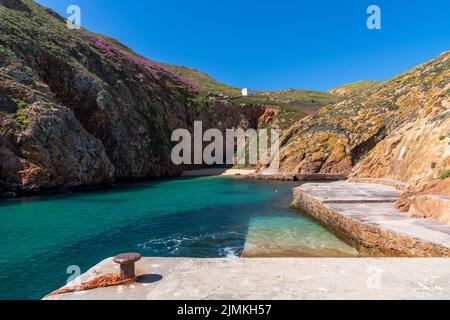 Idyllische Bucht mit kleinem Strand auf einer kleinen atlantischen Insel wirth Klippen und vielen bunten Blumen unter einem blauen Himmel Stockfoto