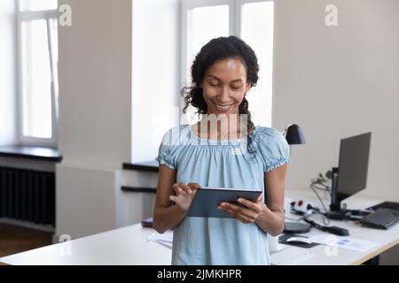 Afrikanische Frau, die an einem digitalen Tablet arbeitet und allein am Arbeitsplatz steht Stockfoto