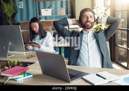 Ein Büroangestellter kann sich auf dem Hintergrund eines Kollegen auf seinem Arbeitsplatz ausruhen Stockfoto