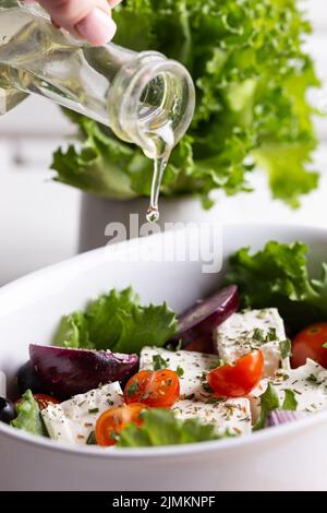 Frau gießt Olivenöl in eine Schüssel mit griechischem Salat Stockfoto