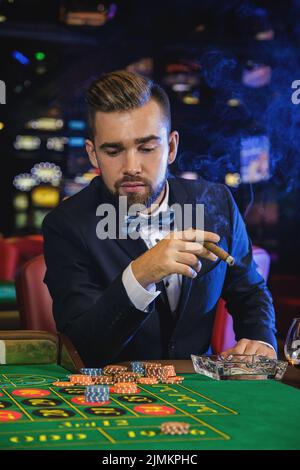 Reicher, gutaussehender Mann, der im Casino Zigarre raucht Stockfoto