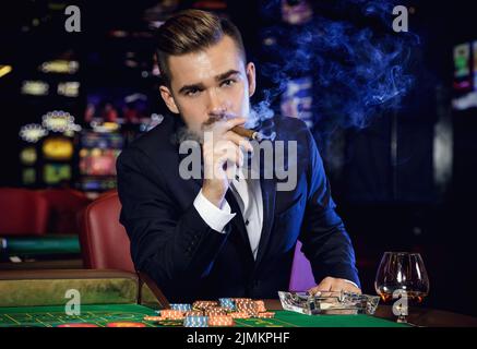 Reicher, gutaussehender Mann, der im Casino Zigarre raucht Stockfoto