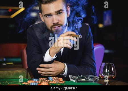 Reicher, gutaussehender Mann, der im Casino Zigarre raucht Stockfoto