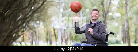 Glücklicher Mann im Rollstuhl dreht den Ball auf seinem Finger im Park Stockfoto