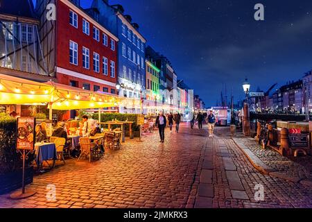 Cafés und Restaurants mit Beleuchtung und bunten Fassaden von alten Häusern auf dem Nyhavn Waterfront Kanal unter dem Nachthimmel wi Stockfoto