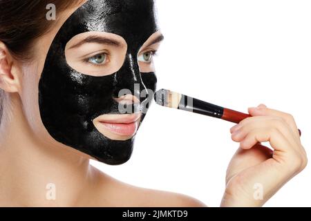 Die schöne Frau wendet eine reinigende schwarze Maske auf ihr Gesicht an Stockfoto