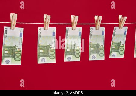 Geldwäsche, Euro-Banknoten hängen am Seil über rotem Studiohintergrund. Stockfoto