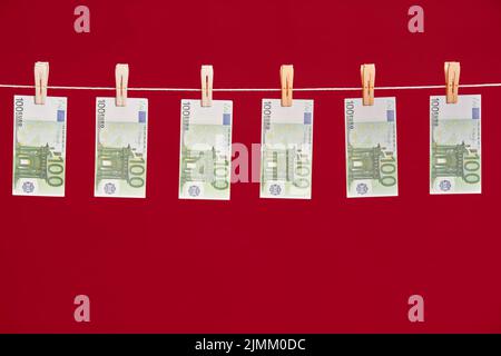 Geldwäsche, Euro-Banknoten hängen am Seil über rotem Studiohintergrund. Stockfoto