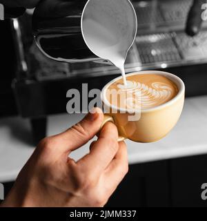 Nahaufnahme einer Tasse Milchkaffee, die von Hand gießt Stockfoto