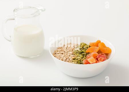 Milch mit gesunden Schüssel Müsli Kürbiskerne trockene Früchte weiße Schüssel weißen Hintergrund Stockfoto