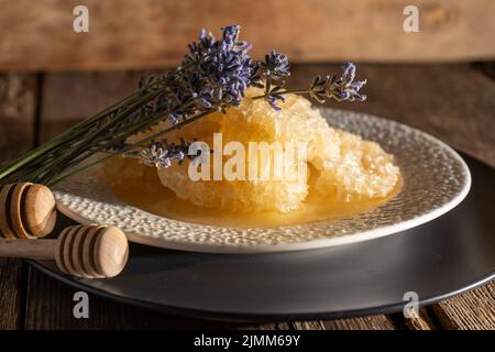 Honig und Waben auf einem weißen Teller. Süßes Essen in einer Schüssel auf dem Tisch. Ein Produkt der Imkerei. Lavendelblüte. Stockfoto