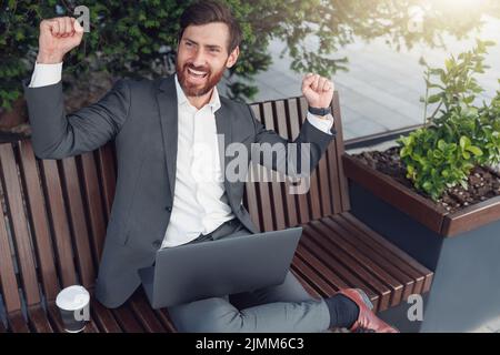 Geschäftsmann freut sich über den Abschluss der Arbeit am Projekt, während er auf der Bank in der Nähe des Büros sitzt Stockfoto