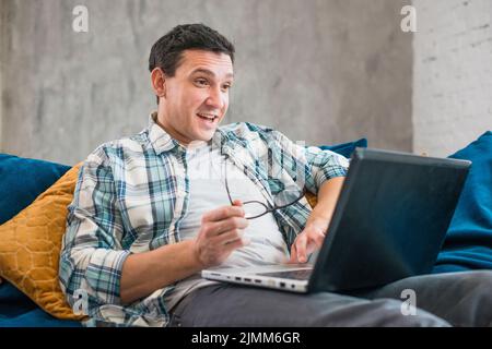 Überraschender Mann, der ein Laptop-Sofa benutzte Stockfoto