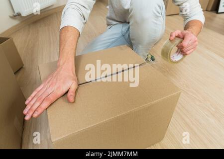 Schließen Sie den männlichen versiegelnden Karton mit Klebeband Stockfoto