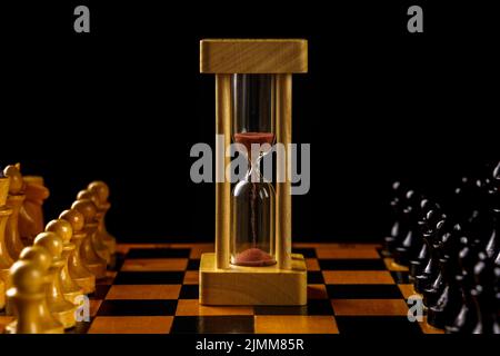 Sanduhr in der Mitte des Schachbretts, schwarze und weiße Stücke. Weichfokus, Copyspace Stockfoto