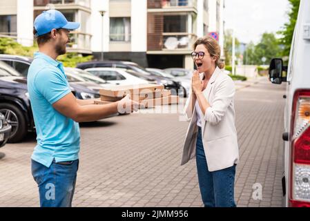 Der Lieferer in blauer Uniform liefert einer Kundin Pizza Stockfoto
