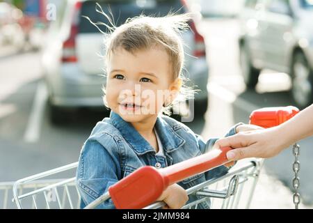 Niedlicher kleiner Junge, der in einem Einkaufswagen sitzt Stockfoto