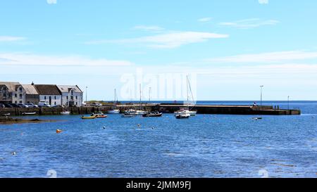 The , Isle of Whithorn, Schottland - 15. Juni 2022: Sonnenbeschienenen Segelbooten und Schlauchbooten, die im Hafen vertäut sind Stockfoto