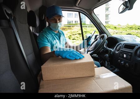 Ein junger Lieferer in einem Lieferwagen überprüft Pakete und Frachtbriefe mit einem Tablet-pc Stockfoto