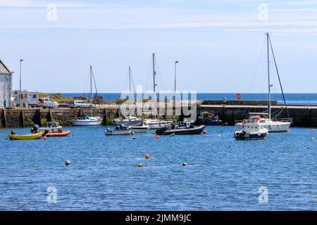 The , Isle of Whithorn, Schottland - 15. Juni 2022: Sonnenbeschienenen Segelbooten und Schlauchbooten, die im Hafen vertäut sind Stockfoto