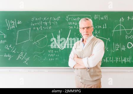 Älterer Professor, der in der Nähe des Klassenzimmers der Schwarzen Tafel steht Stockfoto